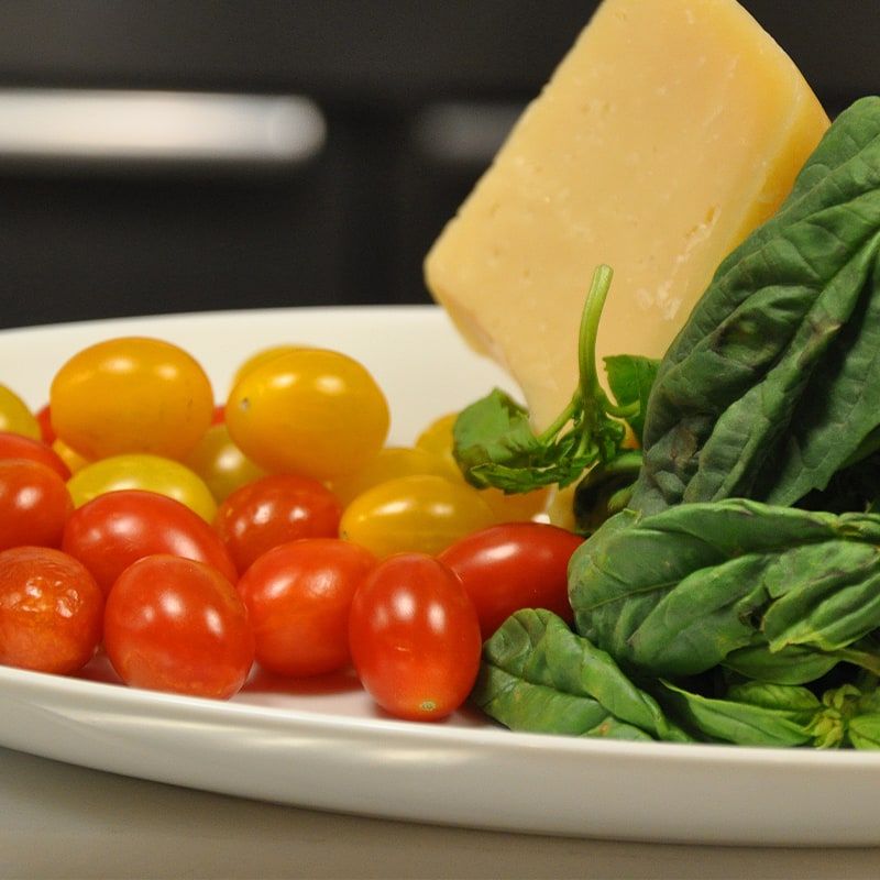 A plate with fresh spinach leaves, a block of cheese, and a mix of yellow and red grape tomatoes, set on a kitchen counter.
