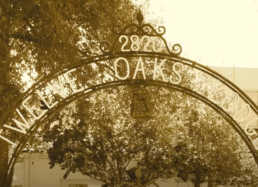 A metal archway sign reads TWELVE OAKS with the number 2820 at the top, surrounded by trees and a lantern hanging from the center. The image has a sepia tone.