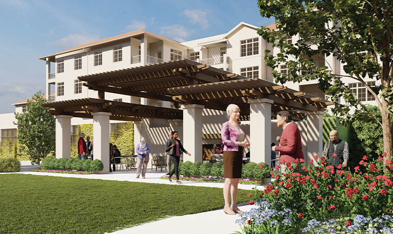 People gather and converse on a sunny day in a landscaped garden outside a modern, multi-story building with a large wooden pergola, surrounded by flowers, trees, and neatly trimmed bushes.