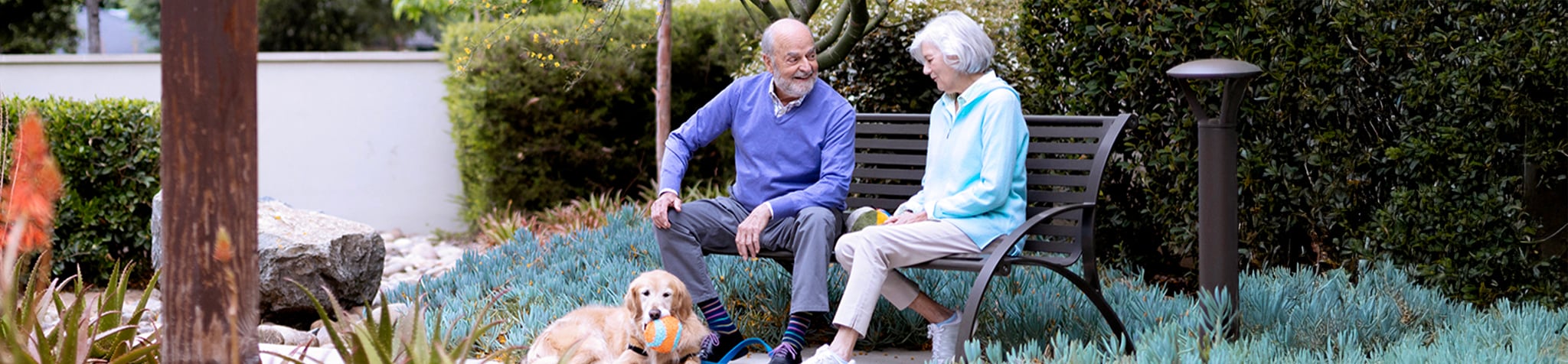two ECS residents share a laugh on park bench while dog lays down in front of them