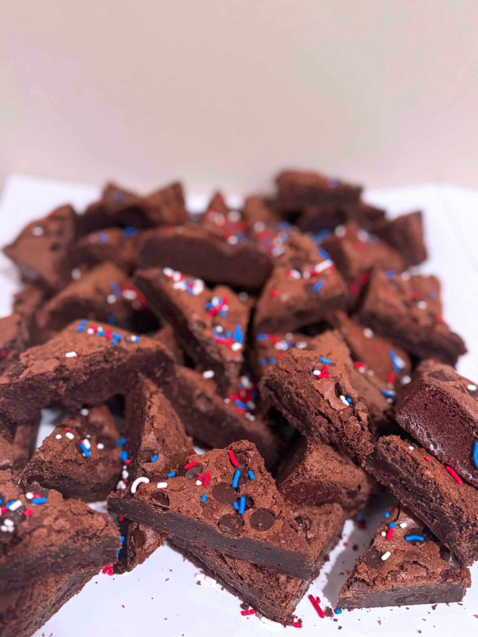 A pile of triangular chocolate brownies topped with red, white, and blue sprinkles, arranged on a white surface.