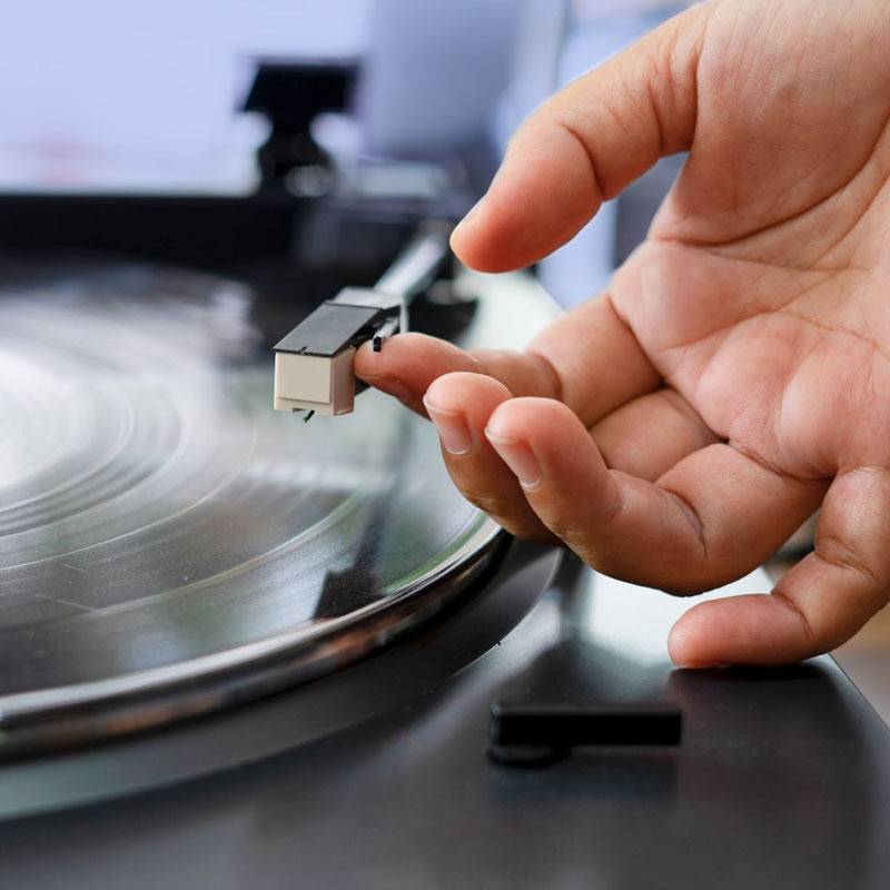A close-up of a hand carefully placing the needle of a turntable onto a spinning vinyl record, preparing to play music.