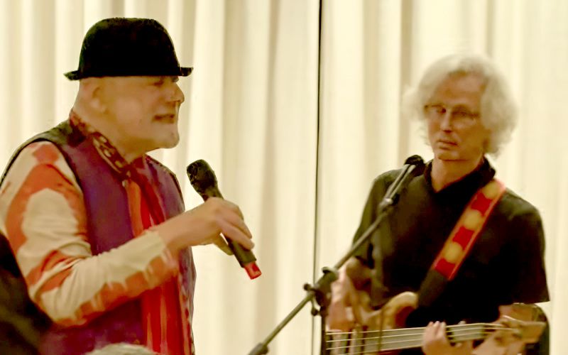 Two men performing on stage with a microphone and guitar.