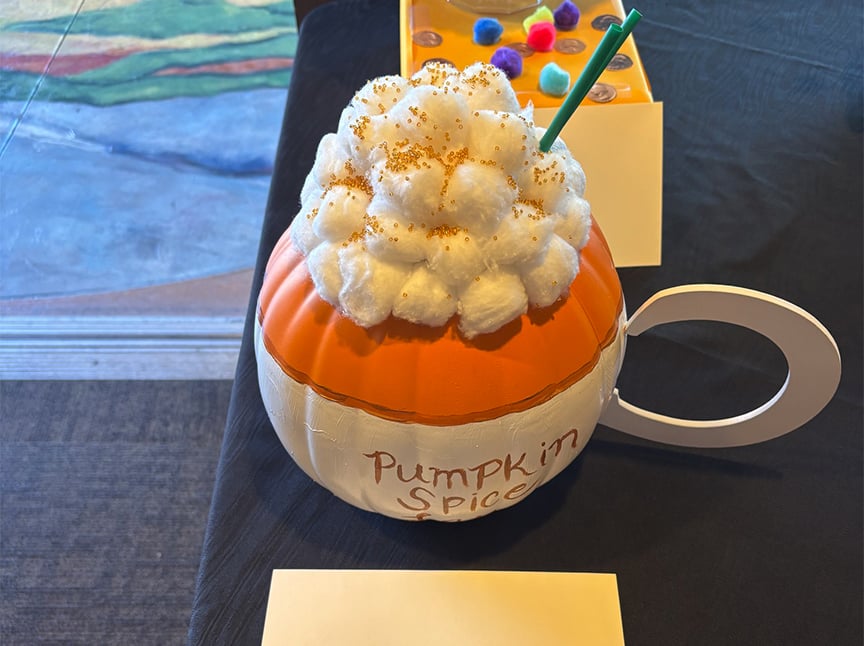 Screenshot A pumpkin painted to look like a pumpkin spice latte, topped with cotton balls as whipped cream and a green straw, with “Pumpkin Spice” written on the side.