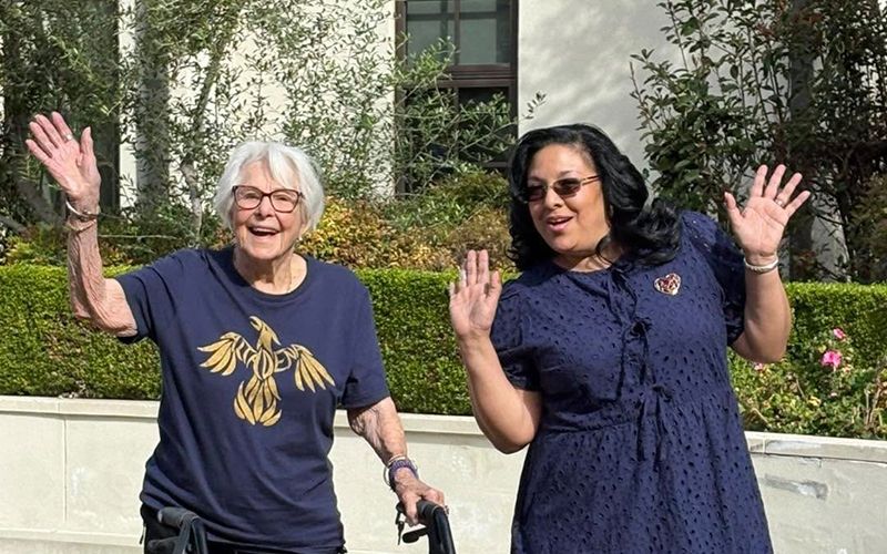 Two women smiling and waving outdoors