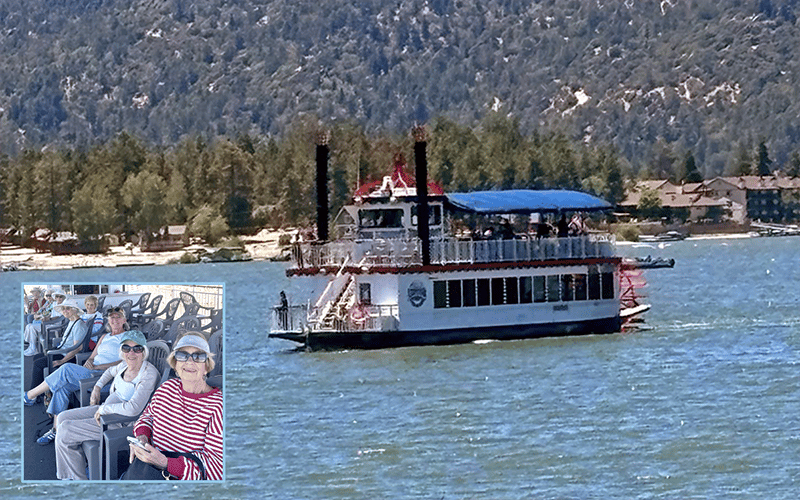 03-Story-4-COV_BigBearLake A paddlewheel boat cruises on a lake near forested hills and lakeside cabins. Inset: a small group of smiling people sit together on the boat, wearing sunglasses and hats.