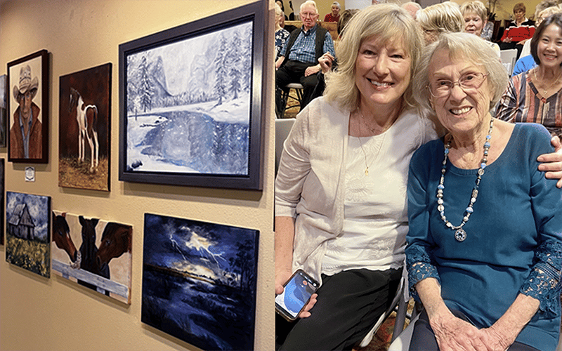04_COV_ResidentArt Two smiling women pose in front of a wall displaying several landscape and animal paintings, including a cowboy portrait, horses, a barn, and a stormy sky.