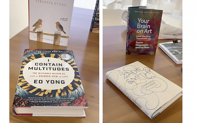 Four books are displayed on a table, including I Contain Multitudes, Your Brain on Art, Changing My Mind, and a partially visible book with birds on the cover titled Virginia Evans.