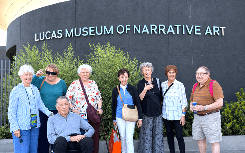 03-Story_04_CAN_ Visit Lucas Museum A group of eight people posing in front of the Lucas Museum of Narrative Art sign.