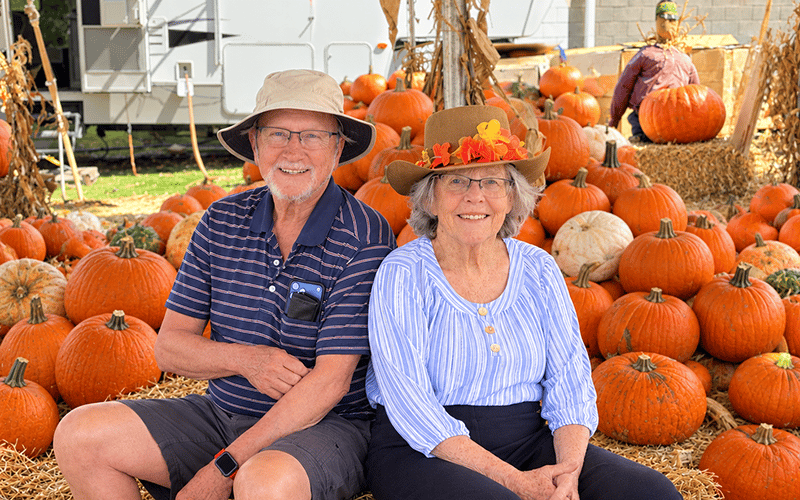 03-Story_05_CAN_PPatch An older couple wearing sun hats sitting on hay bales in front of a large display of pumpkins.