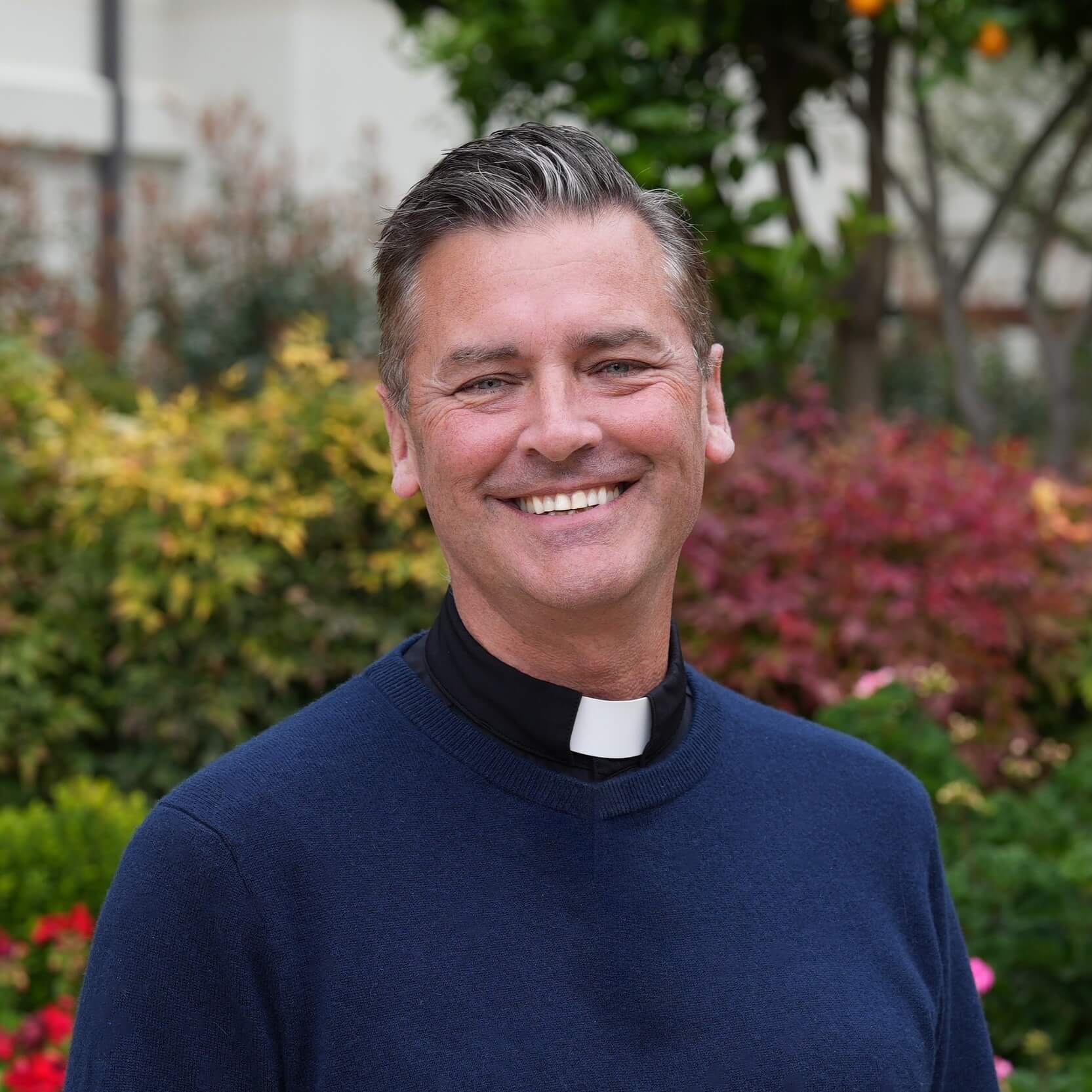 Portrait photograph of Tim Hartley smiling in front of garden