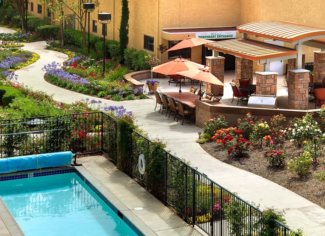 The Canterbury exterior is sprinkled with patio chairs and umbrellas. There also is a pool, surrounded by colorful flowers.