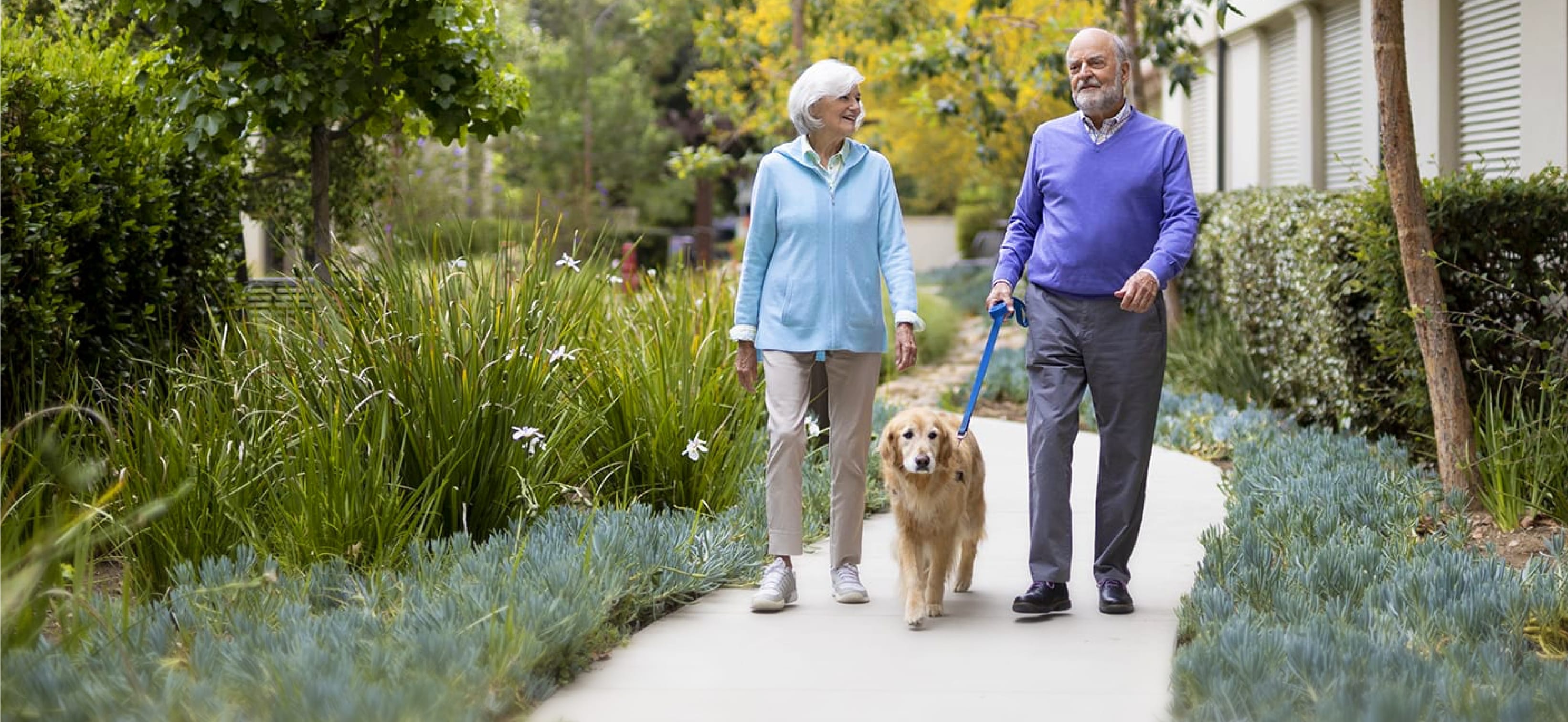man and woman walking dog on senior living garden path