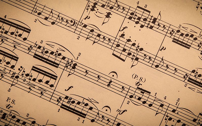 Close-up of vintage sheet music with black musical notes and symbols printed on yellowed paper, arranged diagonally across the image.