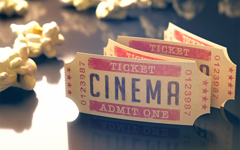 Three vintage-style cinema tickets with Admit One text are displayed on a reflective surface, surrounded by scattered popcorn pieces.