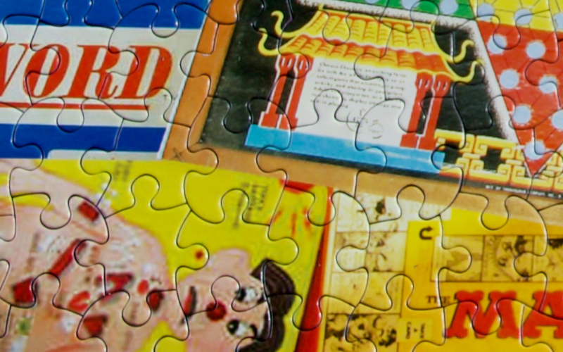 Close-up of a partially completed jigsaw puzzle featuring colorful, vintage-style illustrations and text, including the word WORD, part of a pagoda, and a person’s face. Puzzle piece edges are clearly visible.