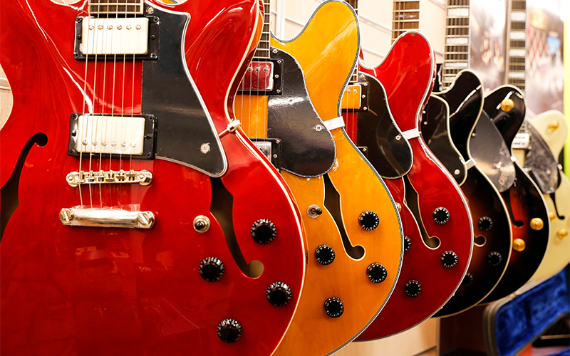 A row of semi-hollow electric guitars in various colors, including red, orange, yellow, and black, hanging on display in a music store.