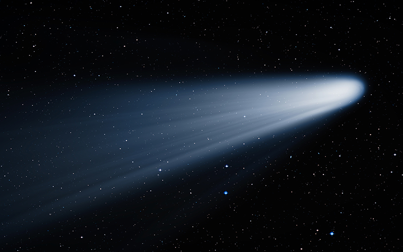 A bright comet with a glowing white tail streaks across a star-filled night sky, its light contrasting against the darkness of space.