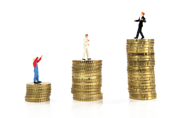 Three miniature figurines in business attire stand on stacks of coins of increasing height, symbolizing income inequality or career progression, against a white background.