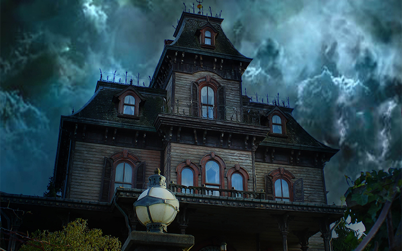 A large, old, dark wooden mansion with pointed roofs and ornate trim stands against a stormy, cloudy sky. A round-topped lamp post is visible in front of the house, adding to the eerie atmosphere.