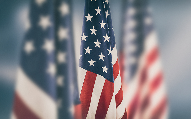 Close-up of a United States flag with stars and stripes, in focus, while two other American flags appear blurred in the background.