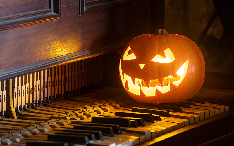 A carved jack-o-lantern with a glowing, menacing face sits on the keys of an old piano, creating a spooky Halloween atmosphere.