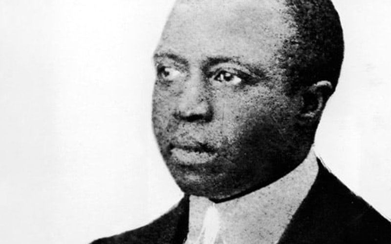 Black and white portrait of a man in a suit and tie, looking slightly to the side with a serious expression, set against a plain background.