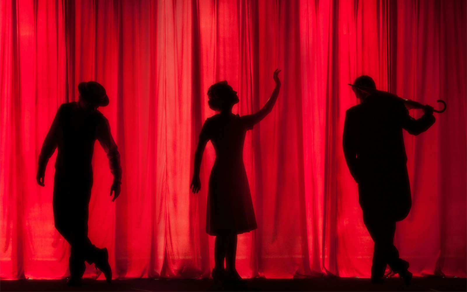 Silhouettes of three performers posing against a bright red curtain.